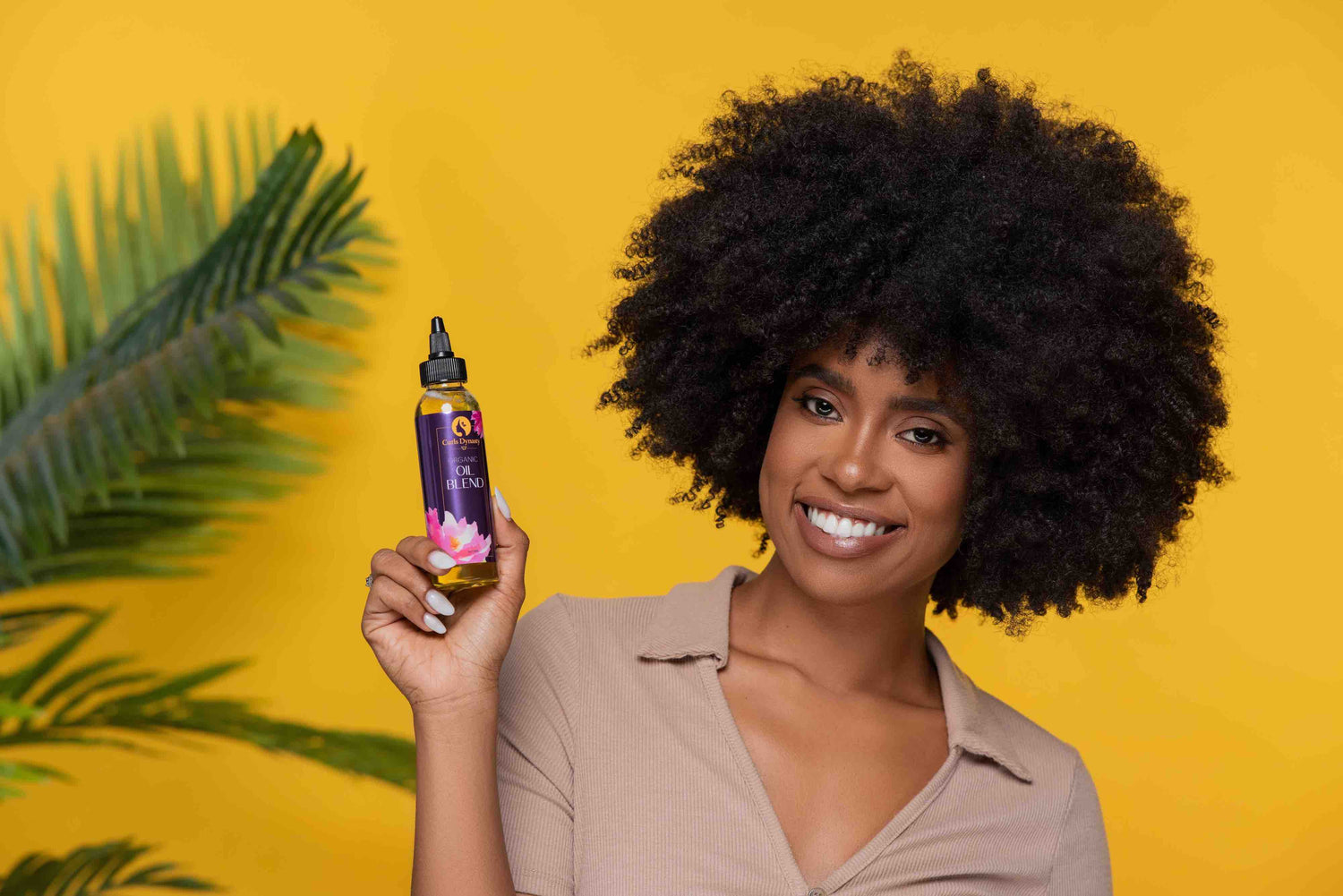 A woman smiling while holding a bottle of organic Oil Blend hair product.