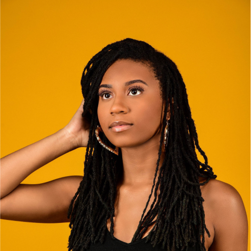A model touching her hair in front of an orange backdrop.