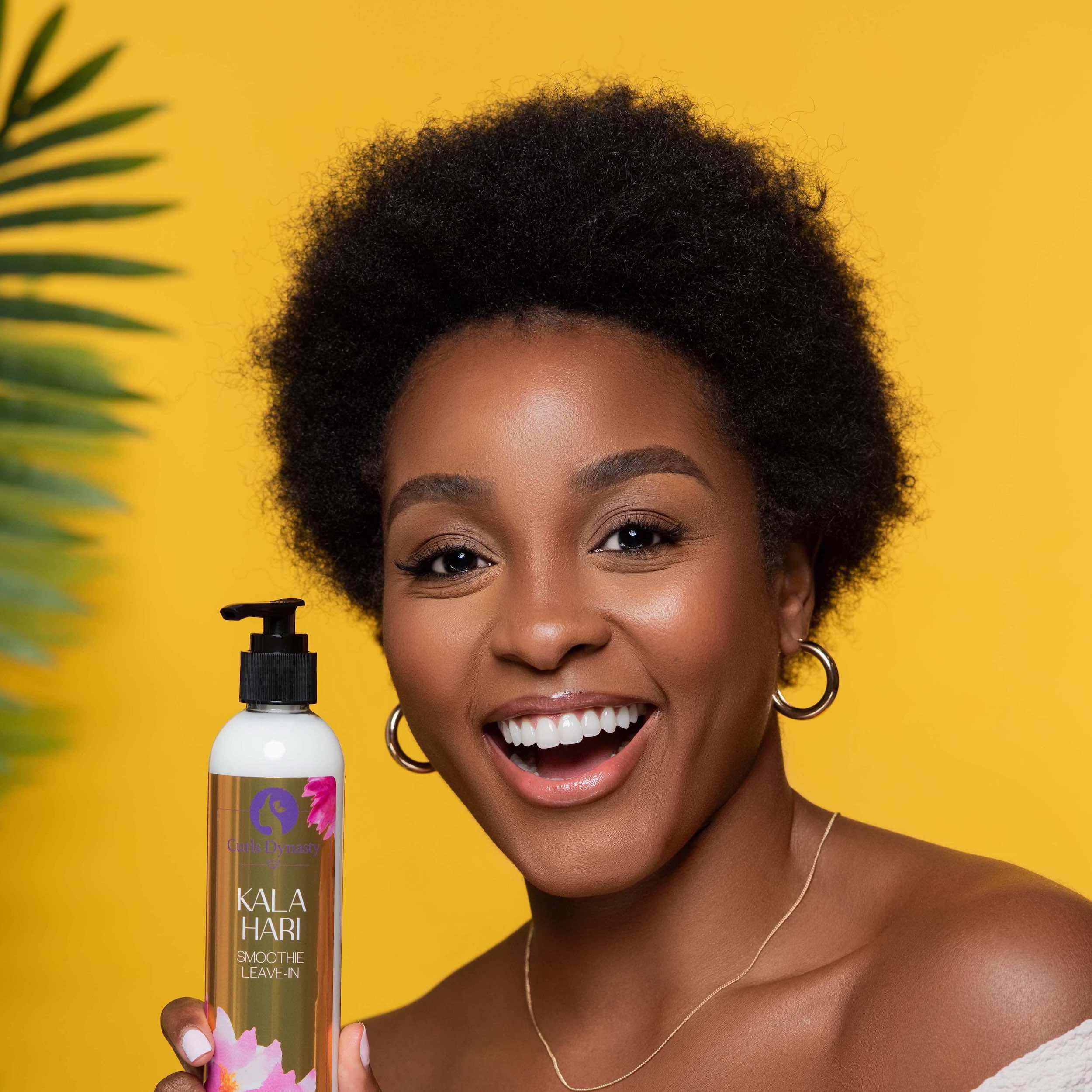 A model smiling while holding a bottle of Kala Hari in front of an orange backdrop.