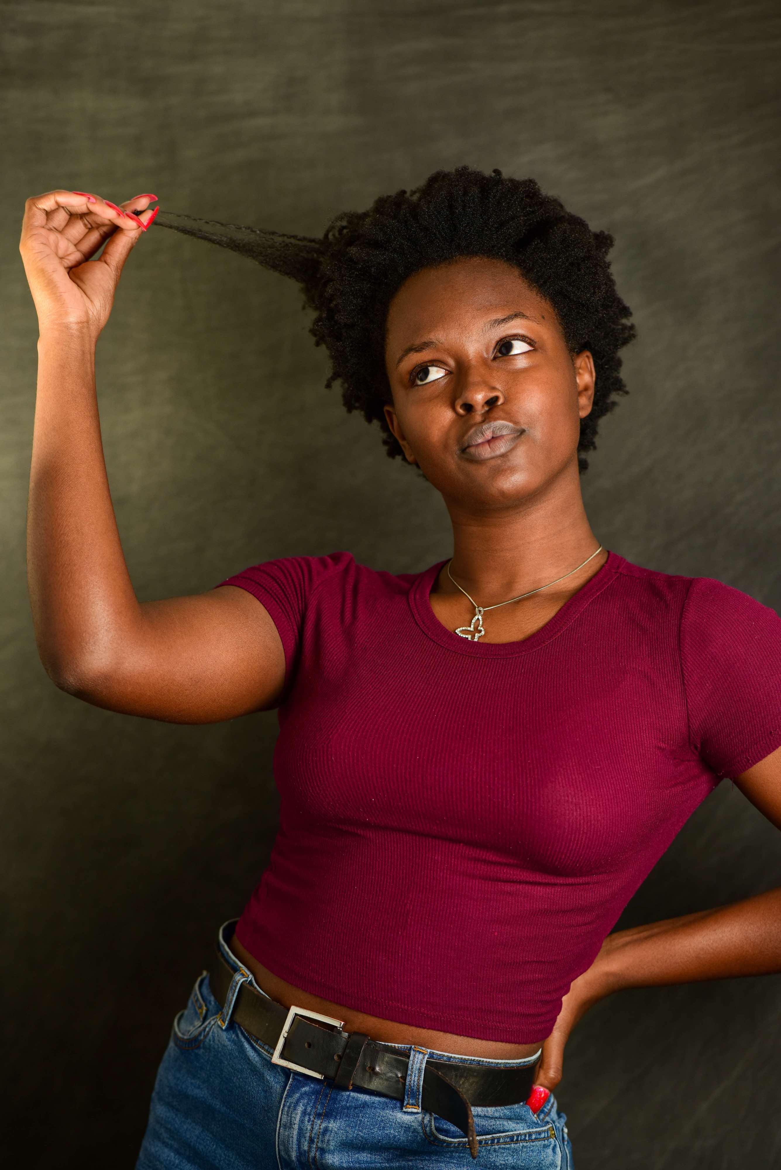 A woman pulling a strand of hair with her hand on her hip.