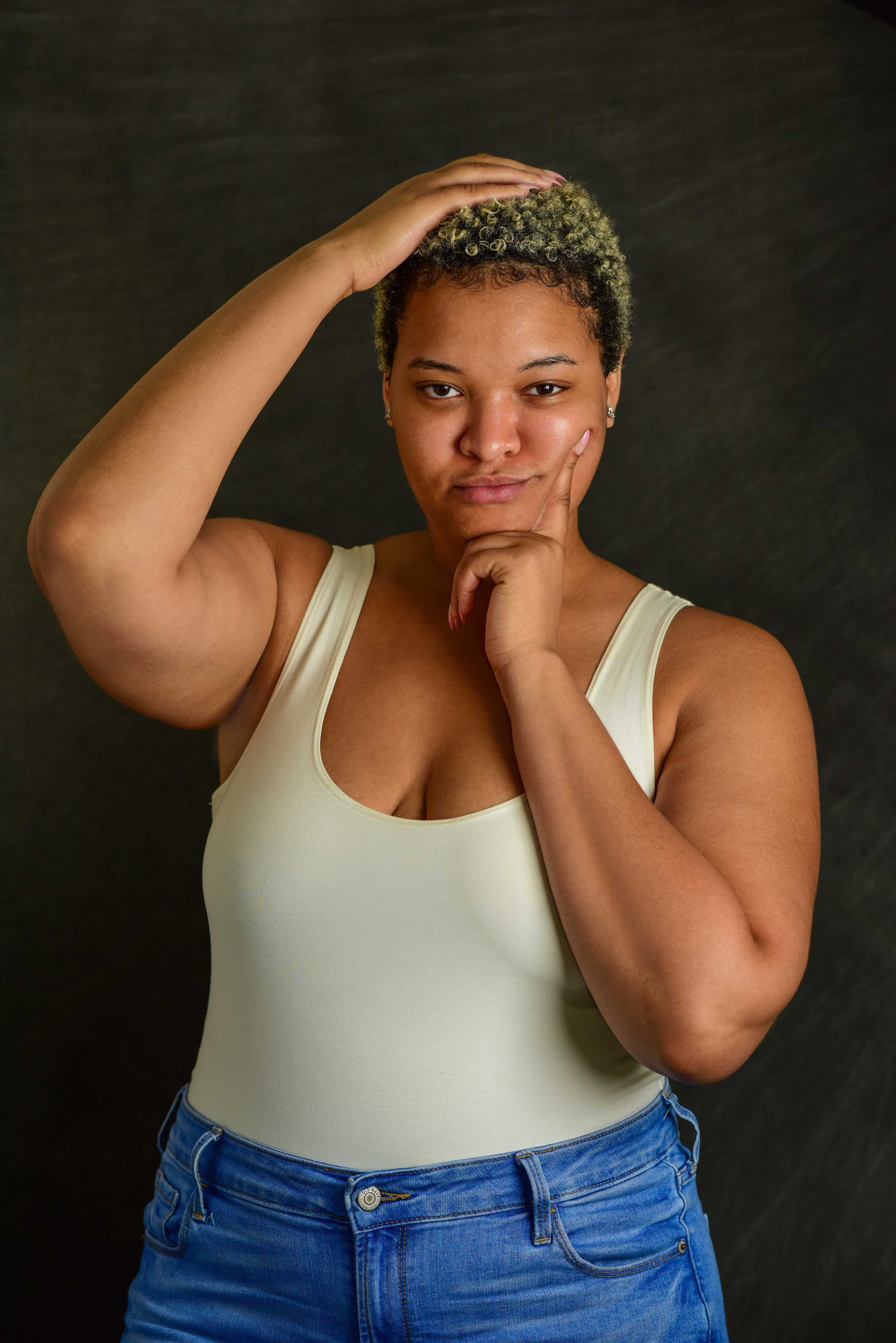 A woman wearing a white tank top touching her hair.