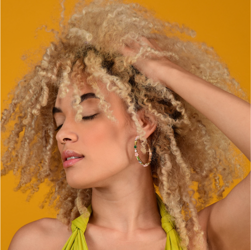 A model with her eyes closed touching her curly hair in front of an orange backdrop.