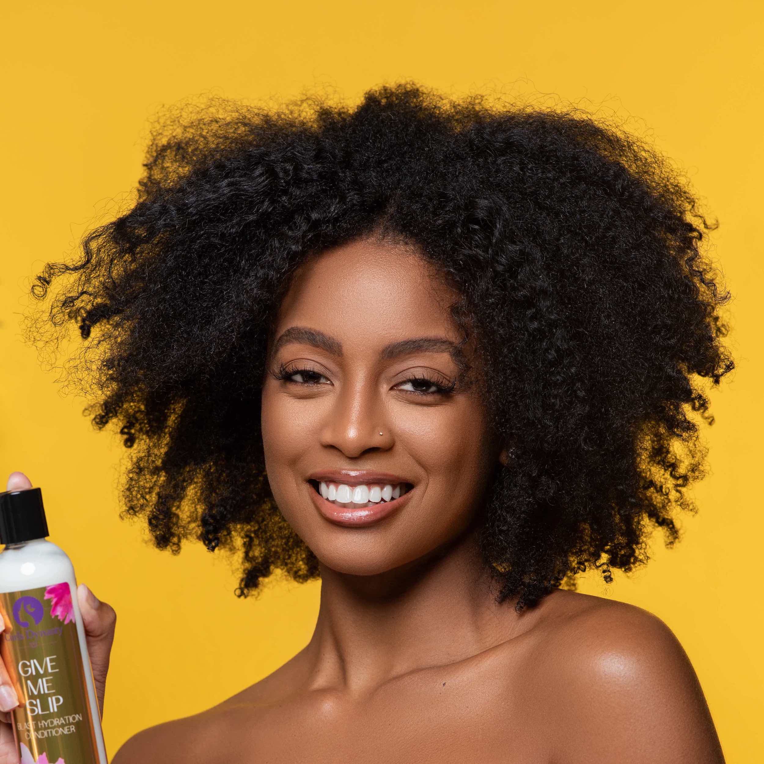 A model smiling while holding a bottle of Give Me Slip in front of an orange backdrop.
